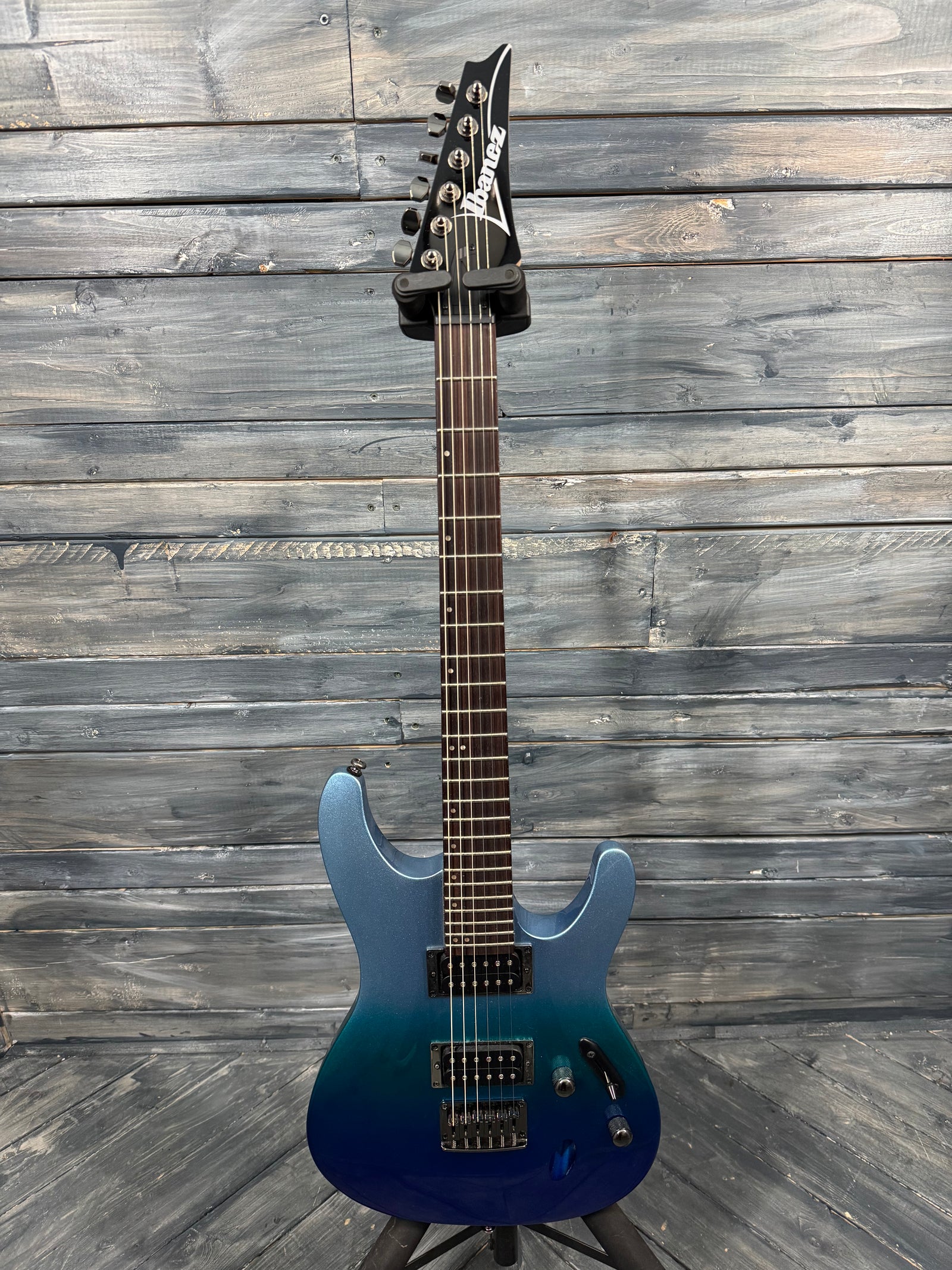 Blue electric guitar on a wooden stand against a wooden wall.