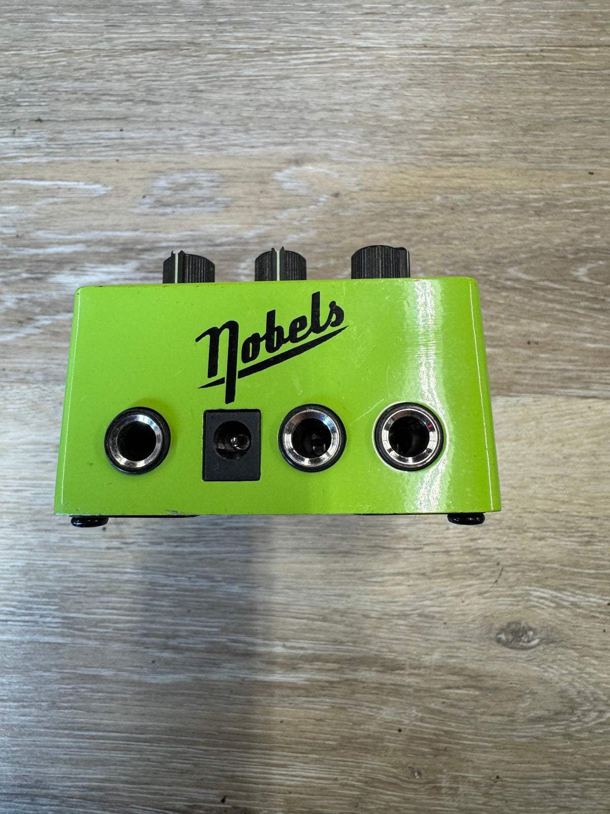 Green guitar effects pedal with 'Nobels' branding on a wooden surface