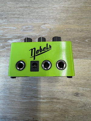 Green guitar effects pedal with 'Nobels' branding on a wooden surface