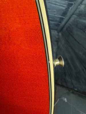 Close-up of a red guitar with a gold fretboard and tuning pegs.