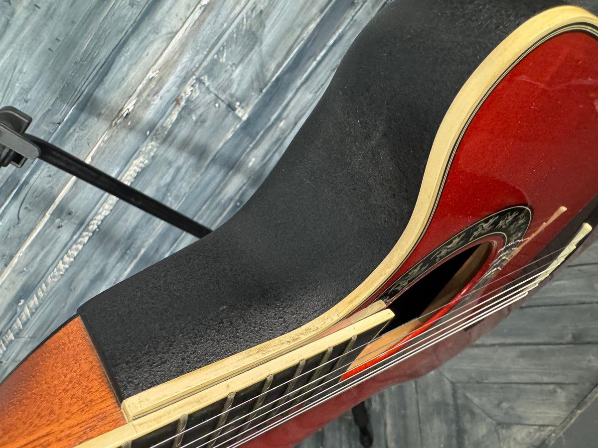 Close-up of a red acoustic guitar with a black pickguard on a textured surface.