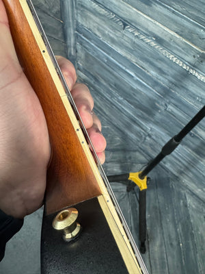 Hand holding a wooden object with a metallic component against a textured wall.