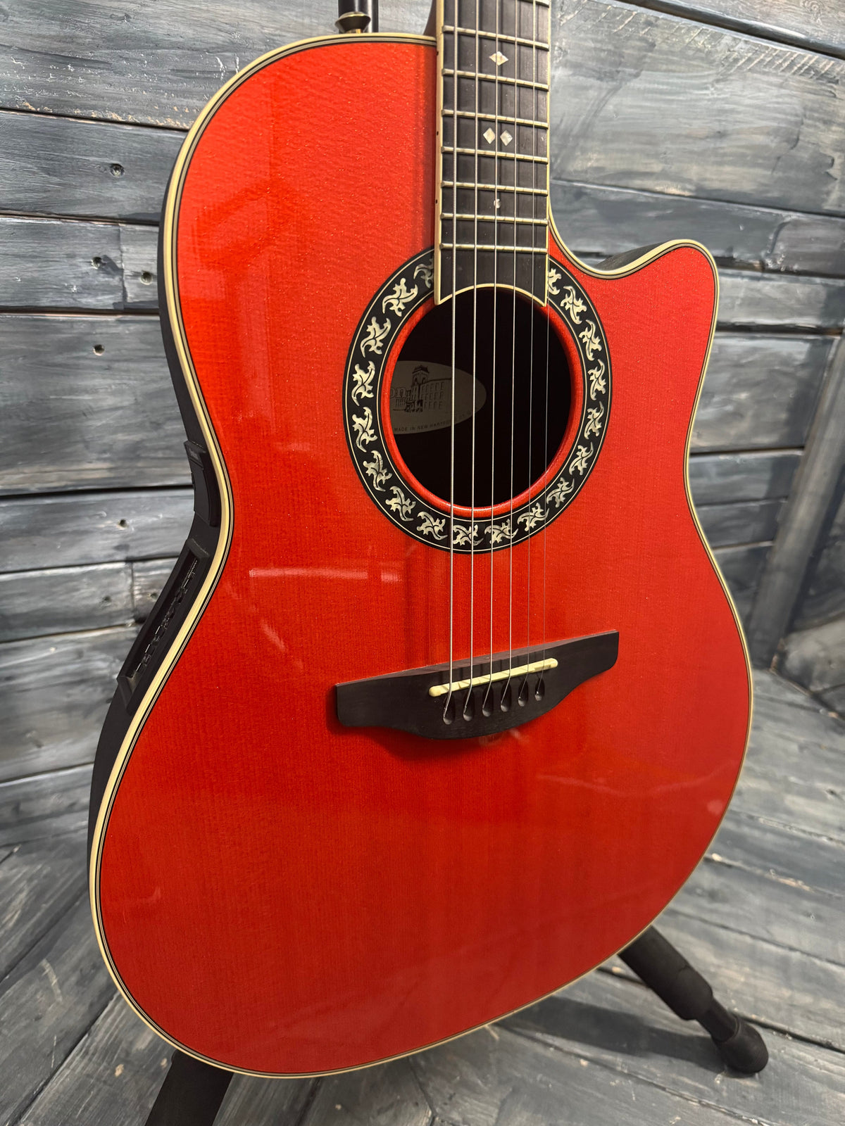 Red acoustic guitar with a decorative soundhole on a wooden floor.
