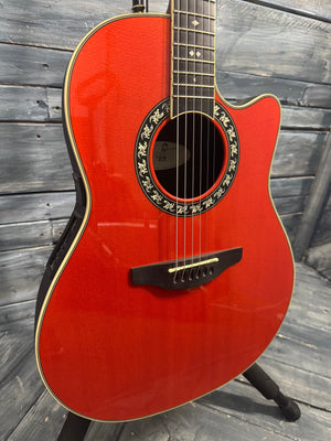 Red acoustic guitar with a decorative soundhole on a wooden floor.