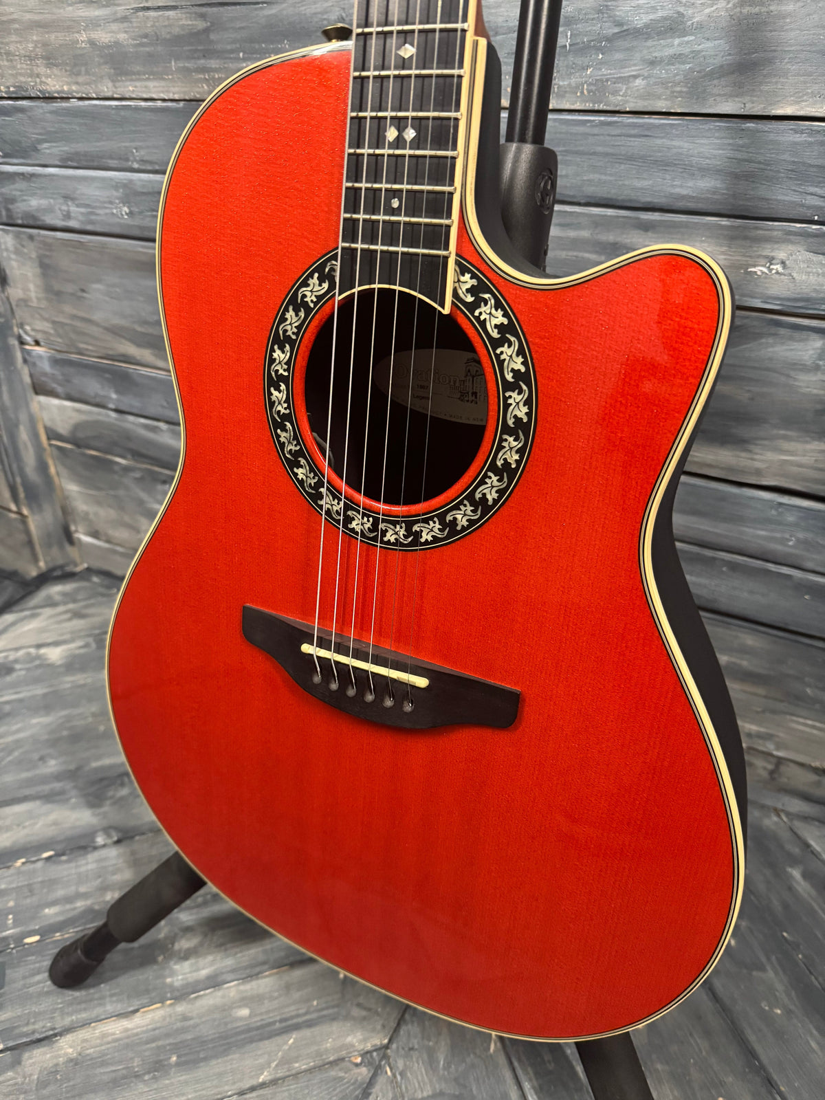 Red acoustic guitar on a wooden stand against a wooden background
