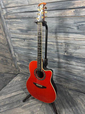 Red acoustic guitar on a stand against a wooden wall.