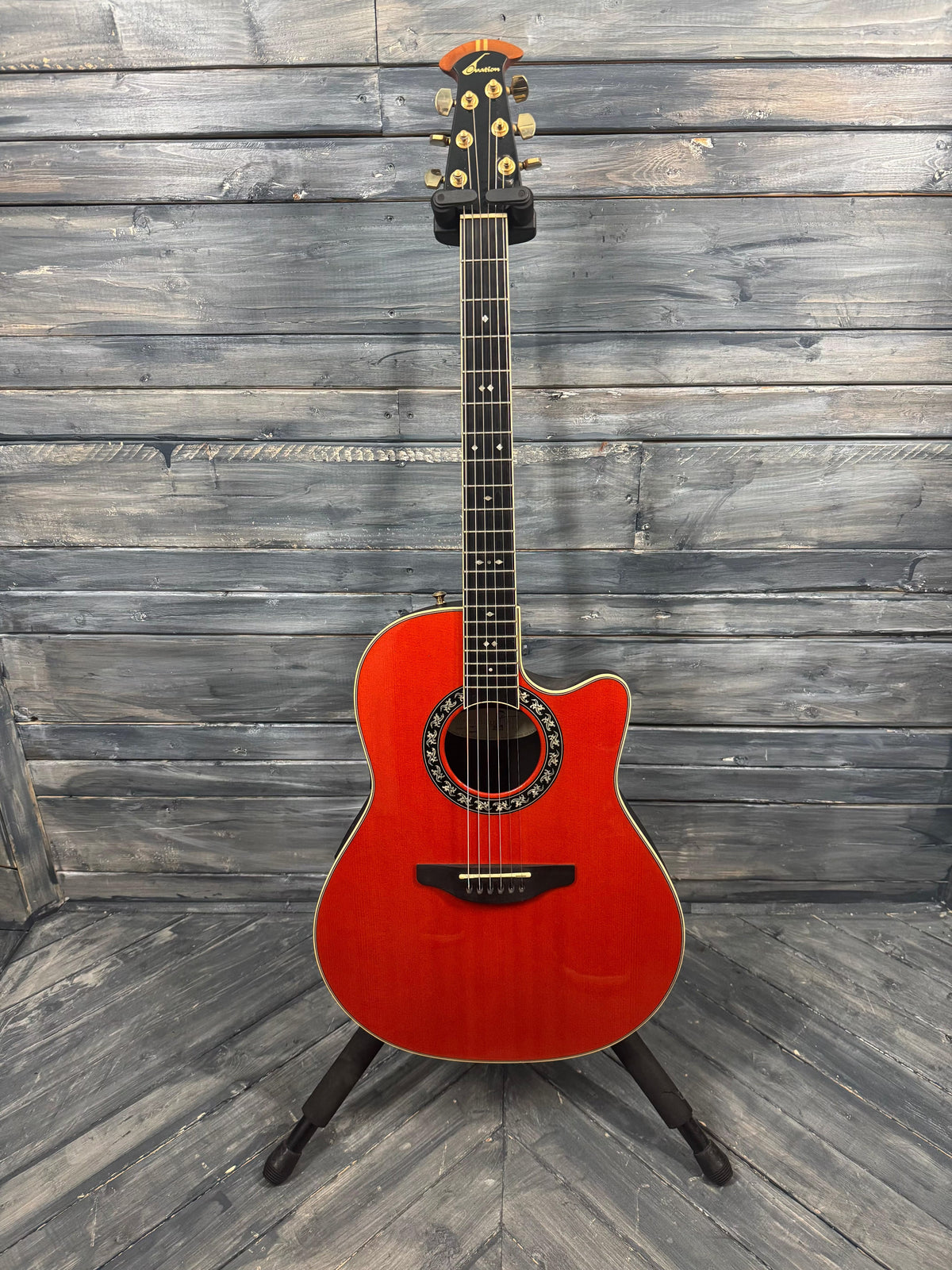 Red acoustic guitar on a stand against a wooden wall.