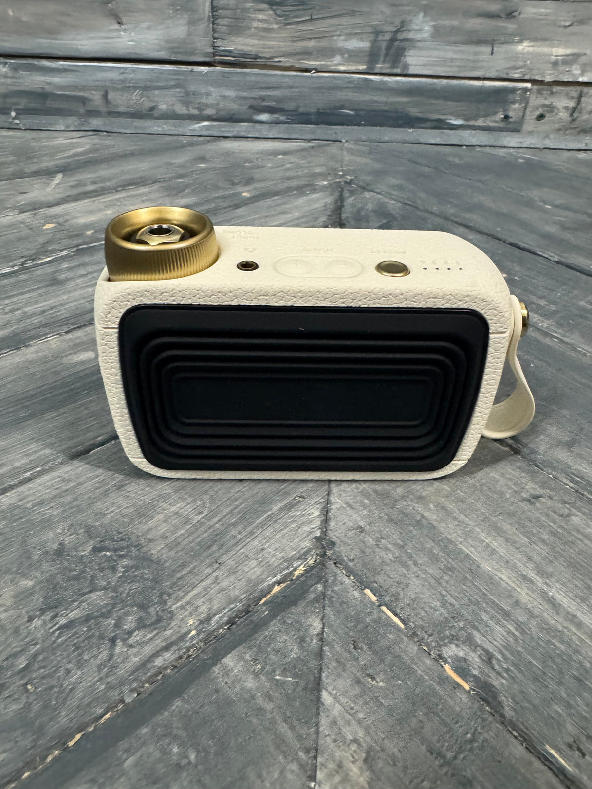 Small rectangular speaker with beige casing and gold accents on a wooden surface