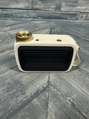 Small rectangular speaker with beige casing and gold accents on a wooden surface
