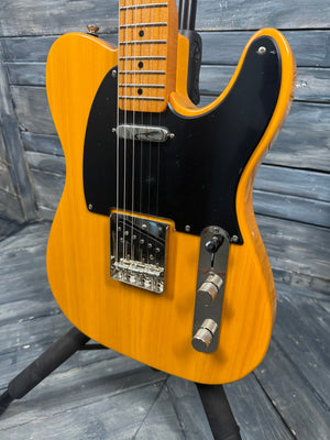 Electric guitar with a blonde finish and black pickguard on a wooden surface
