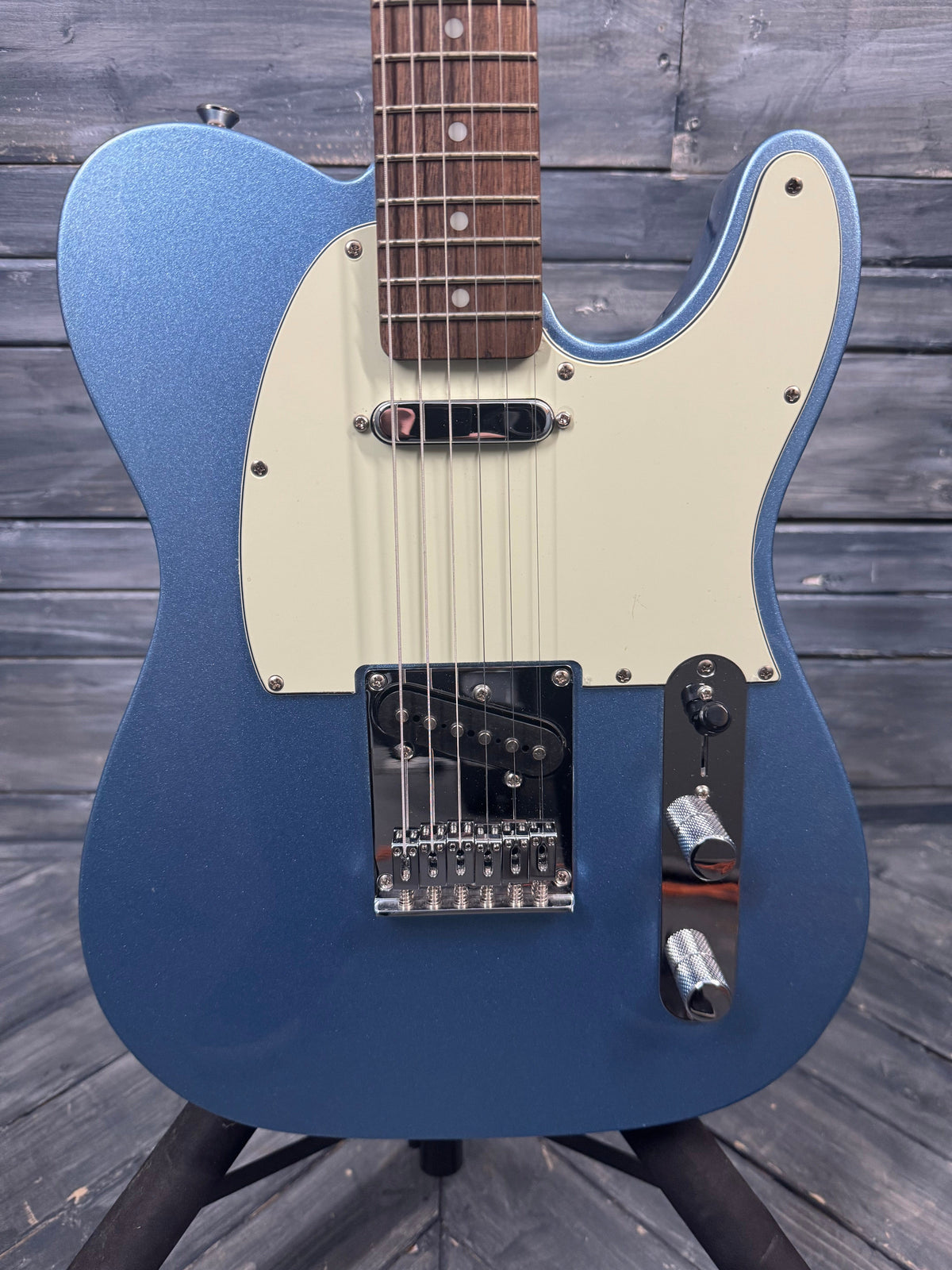 Blue electric guitar with a white pickguard on a wooden surface