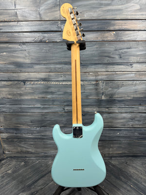 Teal electric guitar on a wooden stand against a wooden wall.