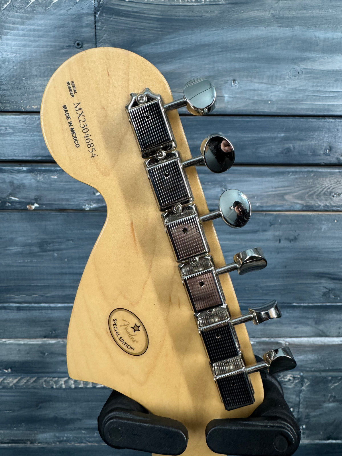 Guitar headstock with tuning pegs on a wooden stand against a wooden background