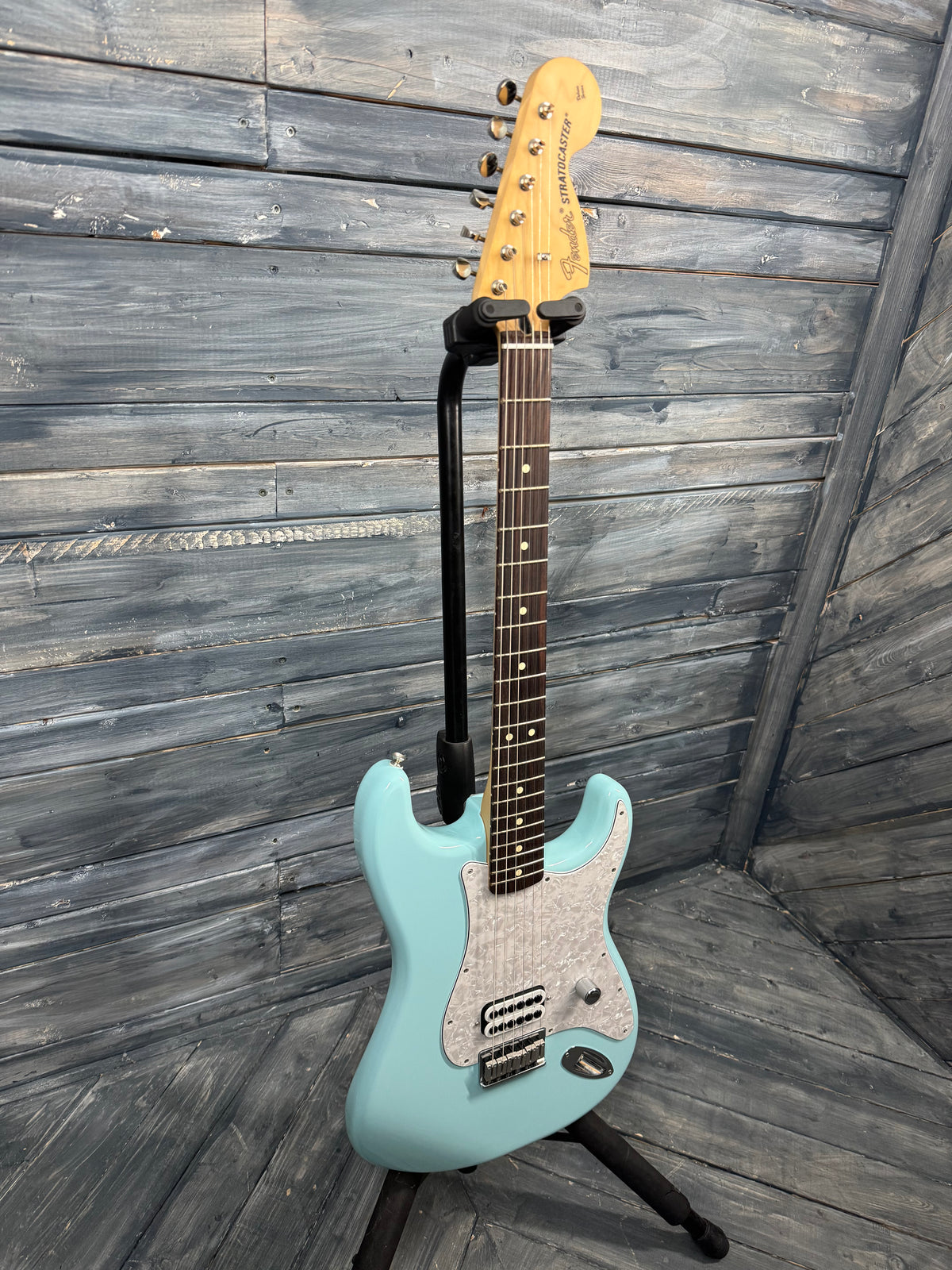 Electric guitar on a stand against a wooden wall