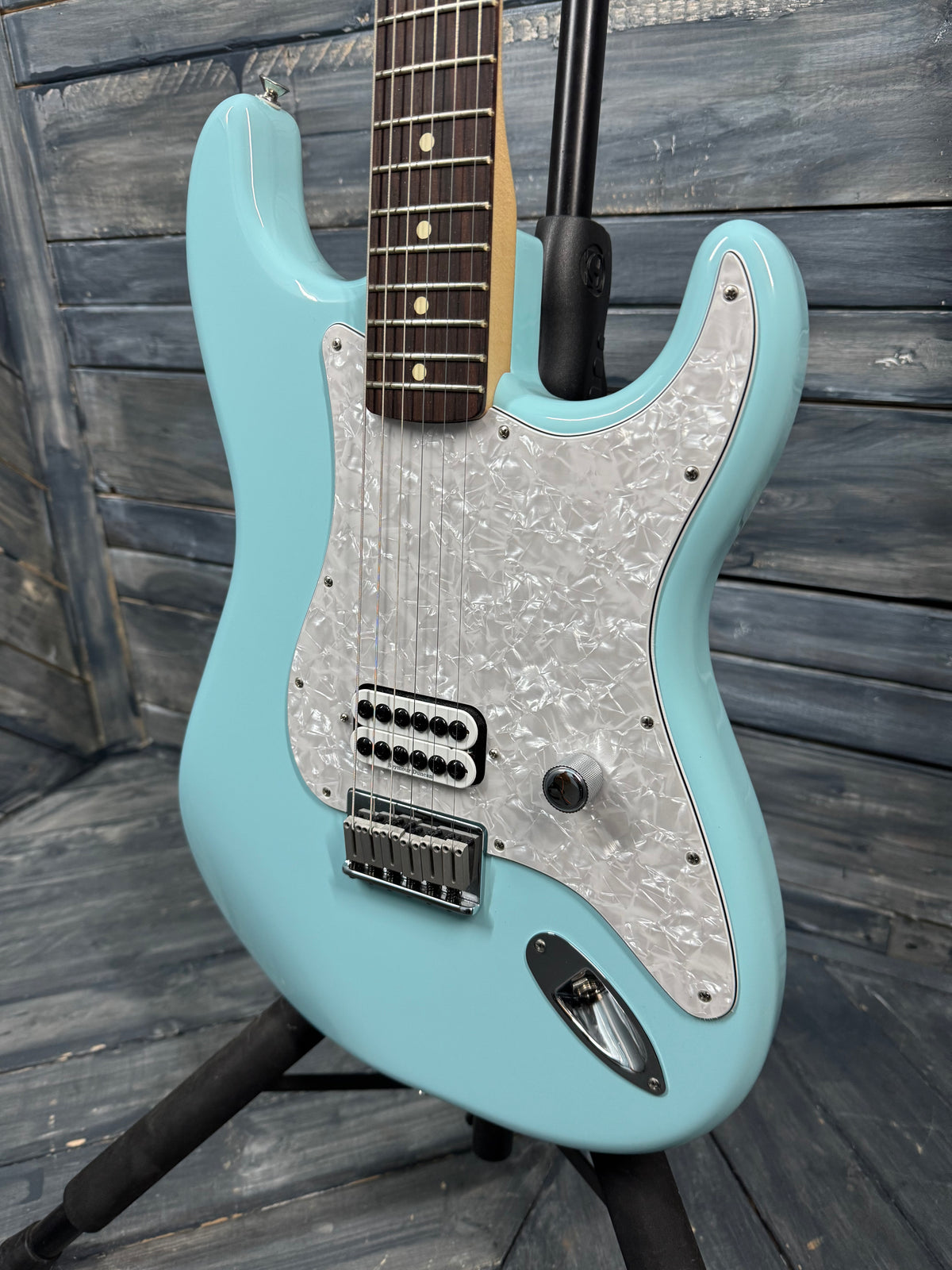 Turquoise electric guitar with a wooden fretboard on a wooden stand against a wooden background