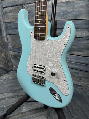Turquoise electric guitar with a wooden fretboard on a wooden stand against a wooden background