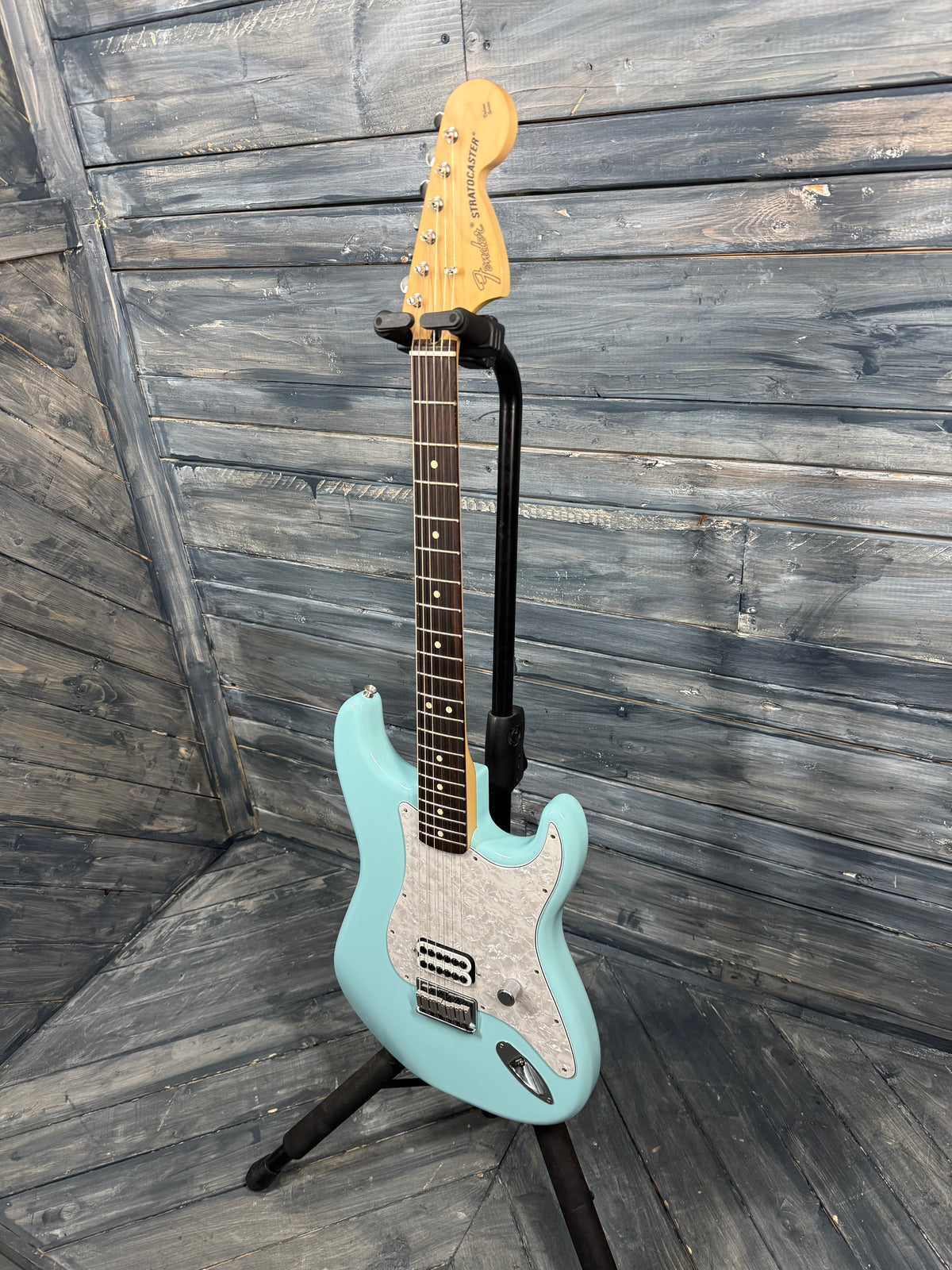 Turquoise electric guitar on a stand against a wooden wall.