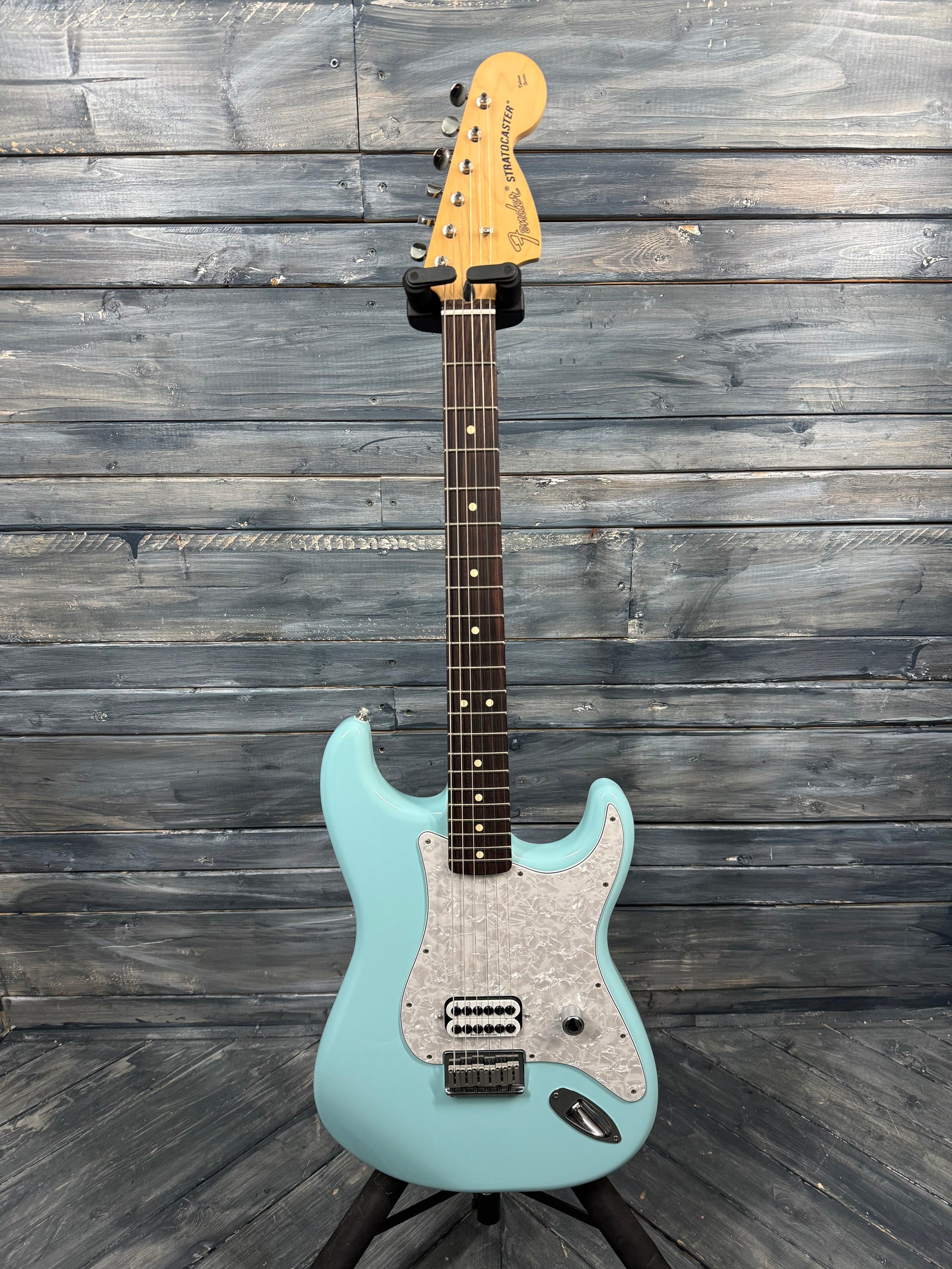 Teal electric guitar on a stand against a wooden wall