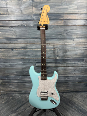 Teal electric guitar on a stand against a wooden wall