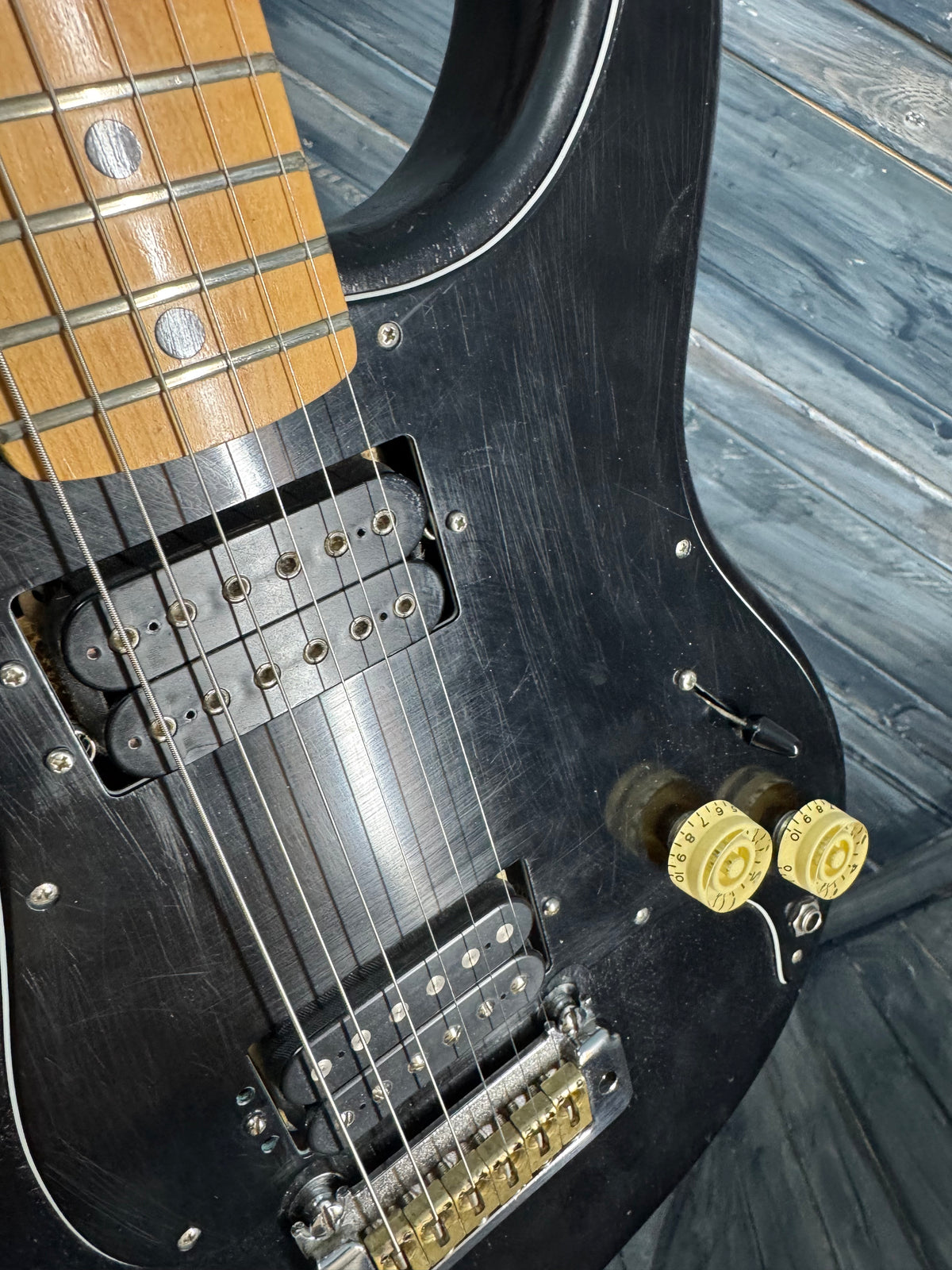 Close-up of a black electric guitar with gold hardware on a wooden surface