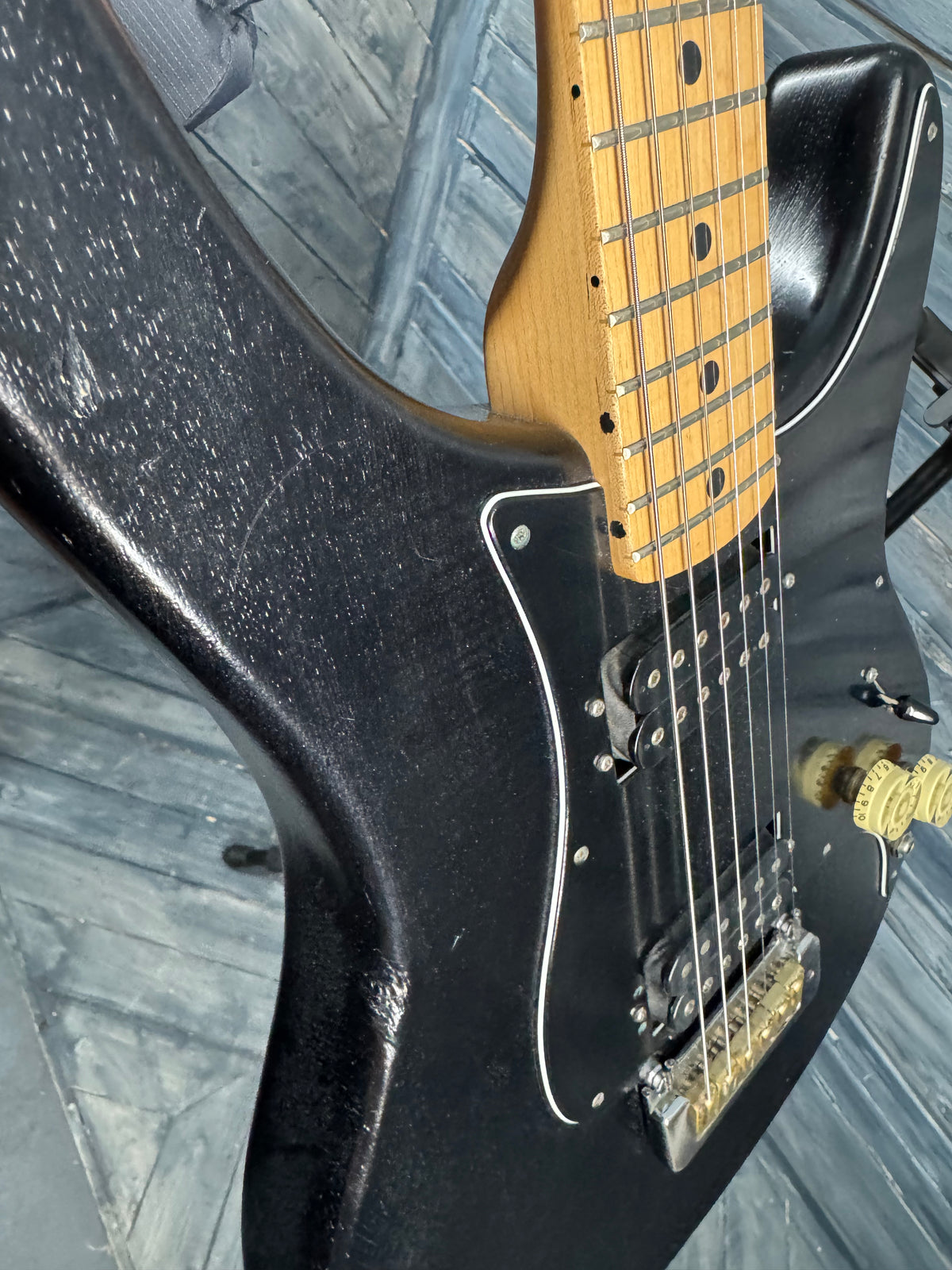 Close-up of a black electric guitar with a wooden fretboard on a reflective surface.
