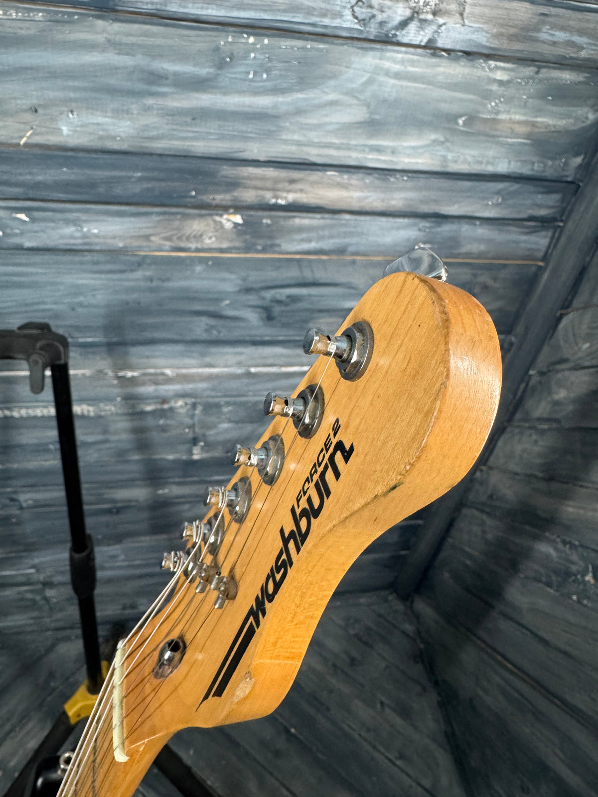 Wooden guitar headstock with 'Gotoh' branding against a wooden wall.