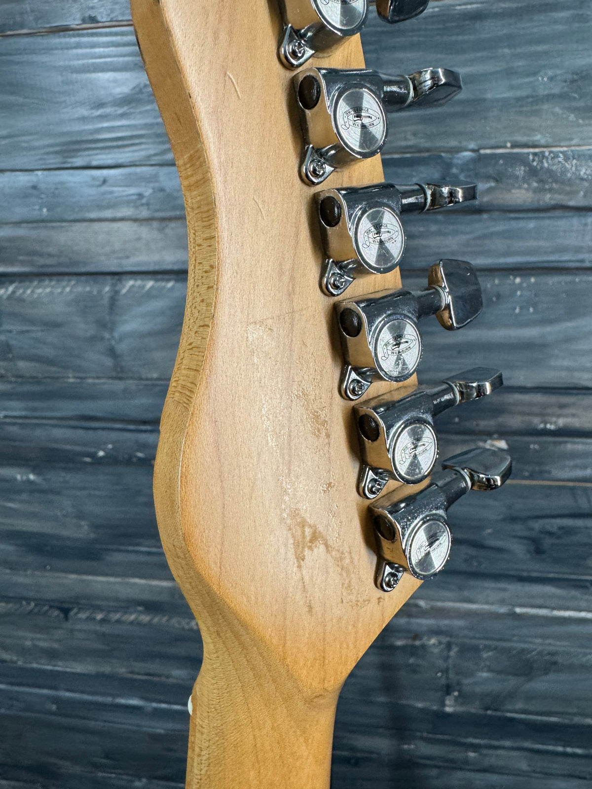 Close-up of a guitar neck with tuning pegs against a wooden background
