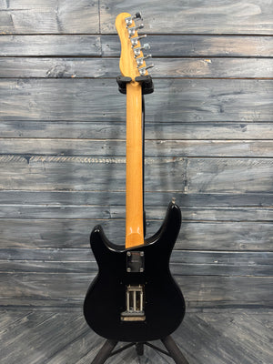 Black electric guitar with a wooden neck against a wooden background
