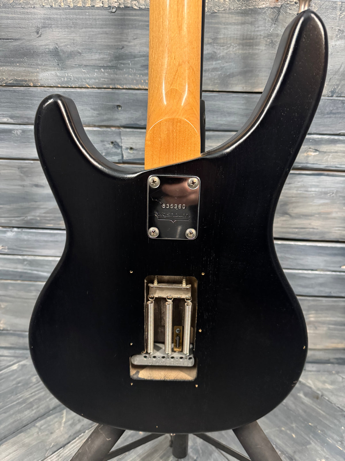 Black electric guitar with a wooden neck against a wooden background