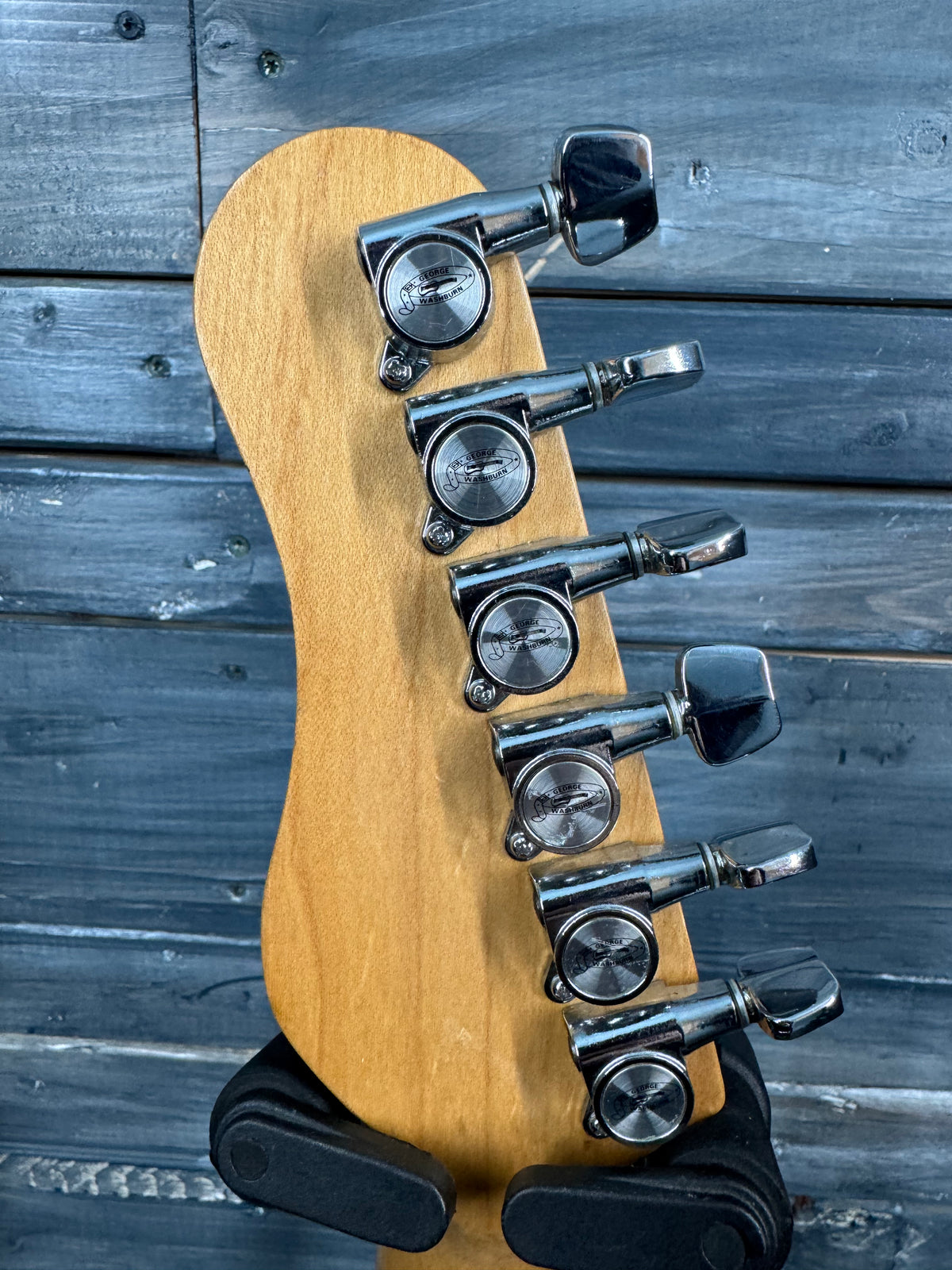 Guitar headstock with tuning pegs on a wooden stand against a wooden background