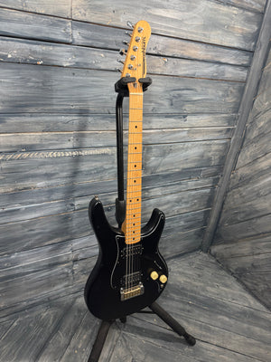 Black electric guitar on a stand against a wooden wall.