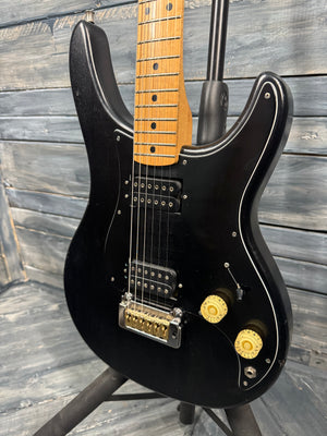 Black electric guitar with a wooden fretboard against a wooden background