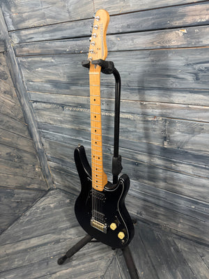 Black electric guitar on a stand against a wooden wall.