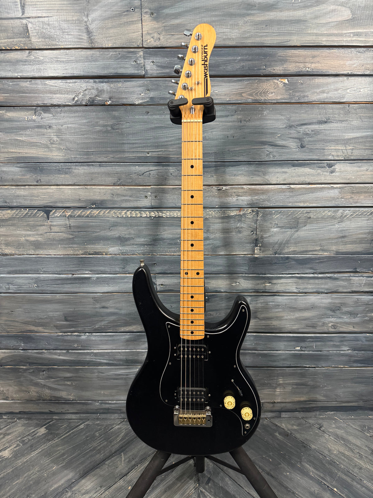 Black electric guitar with a maple neck against a wooden background