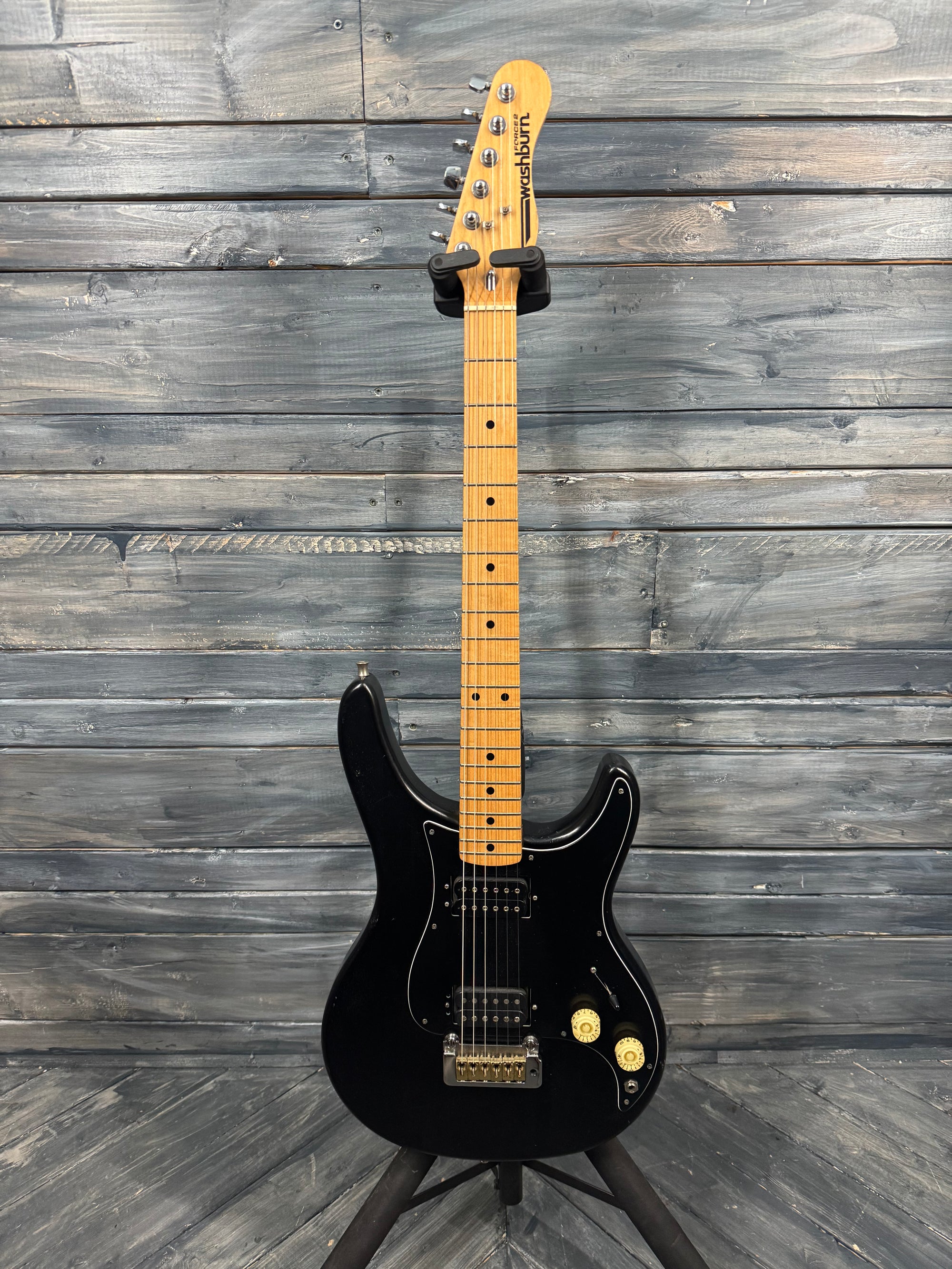 Black electric guitar with a maple neck against a wooden background