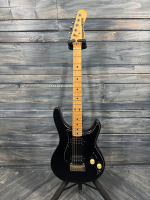 Black electric guitar with a maple neck against a wooden background