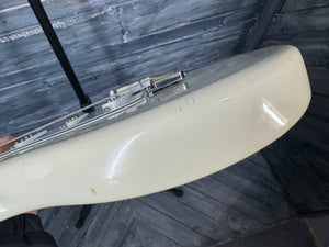 Close-up of a white curved object with a metallic component on a wooden floor.