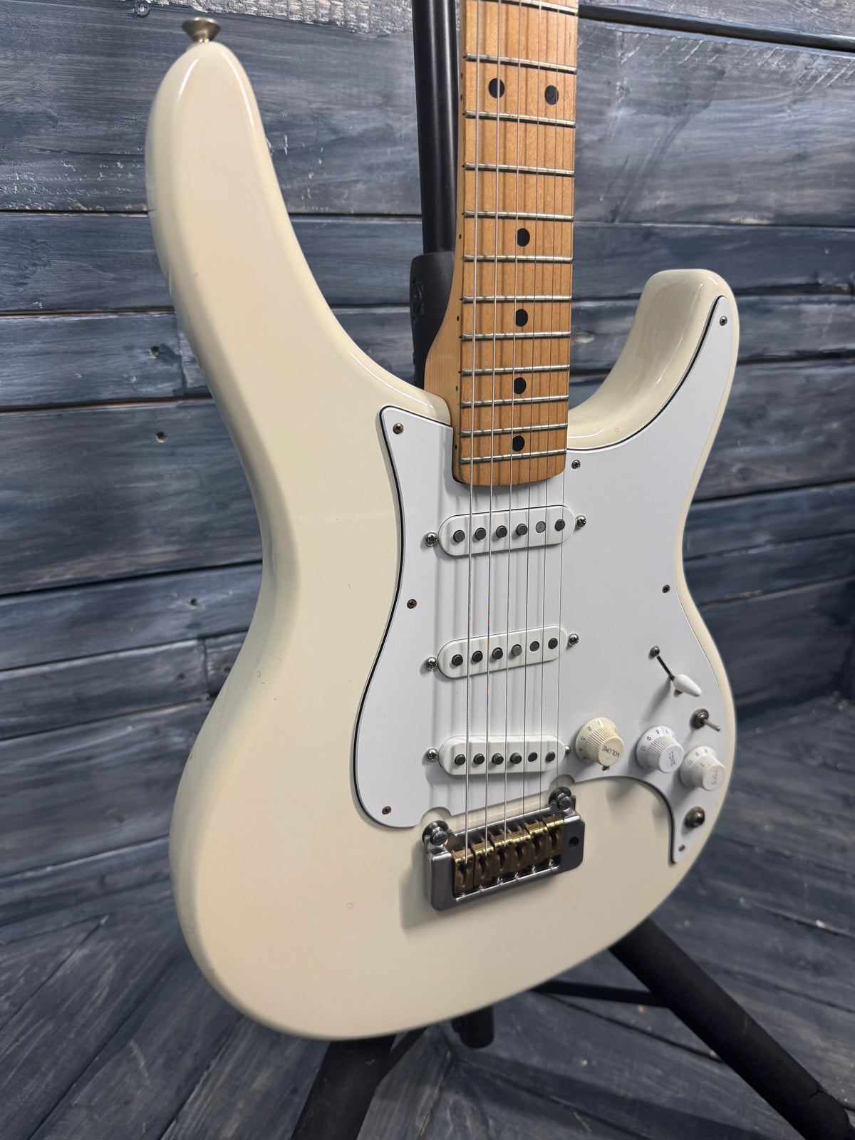 Beige electric guitar with a wooden fretboard against a wooden background