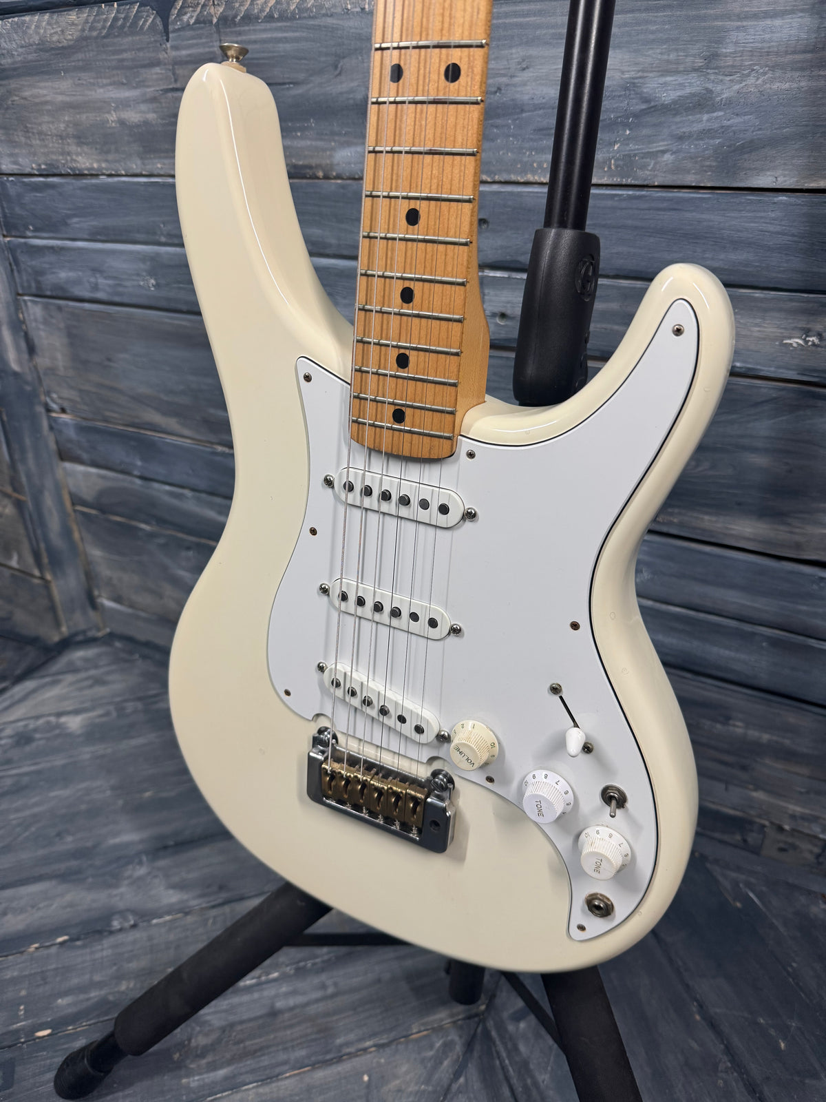 White electric guitar with a wooden fretboard on a stand against a wooden background