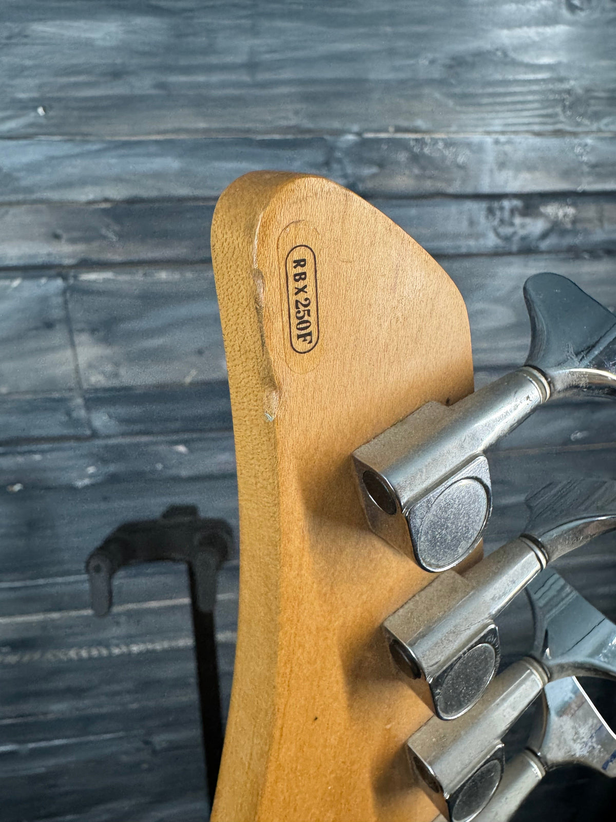Wooden guitar neck with metal tuning pegs on a wooden background