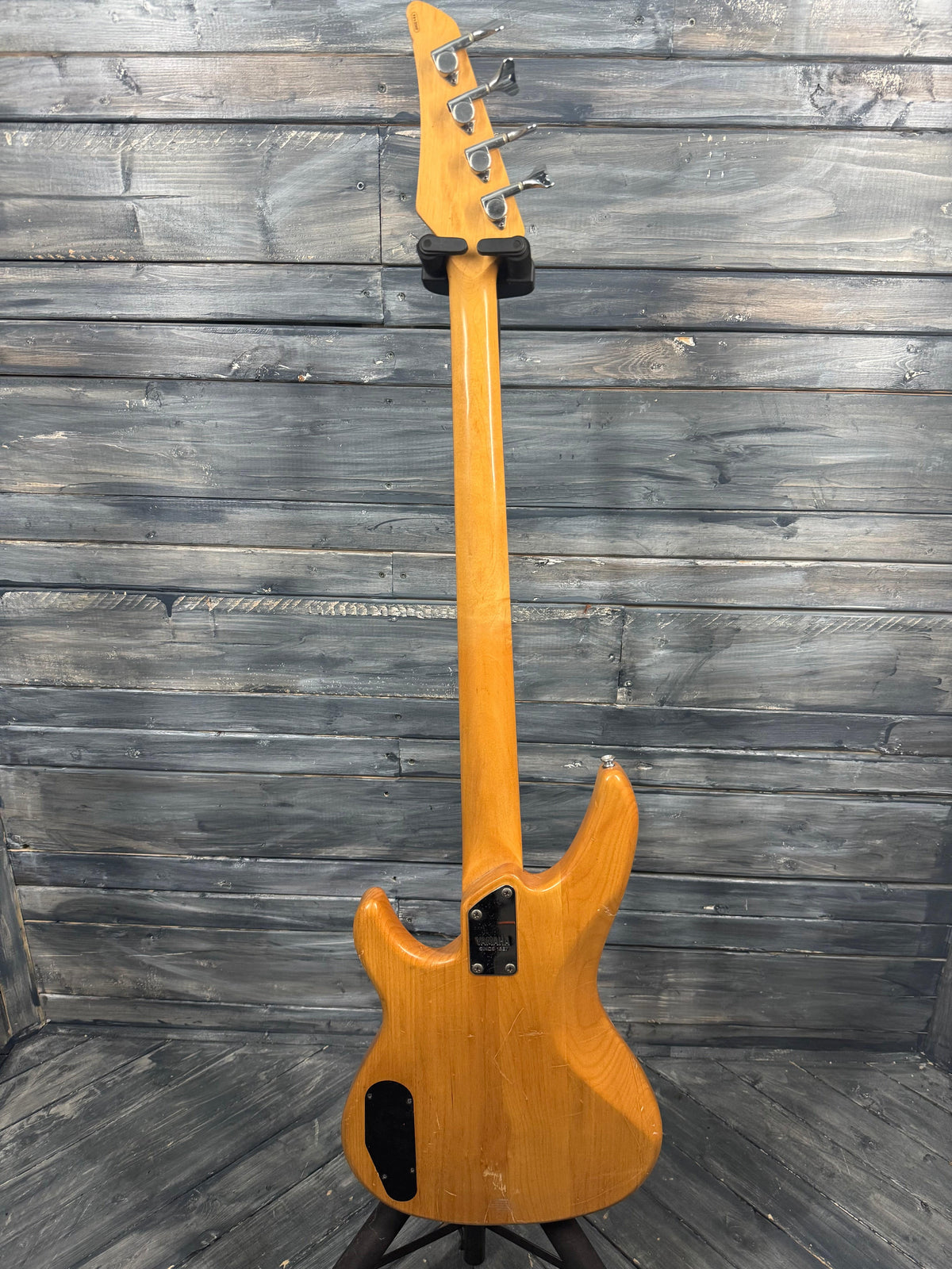 Electric bass guitar with a wooden finish leaning against a wooden wall.