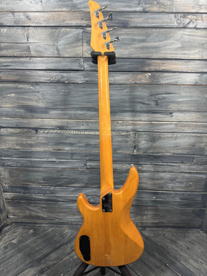 Electric bass guitar with a wooden finish leaning against a wooden wall.