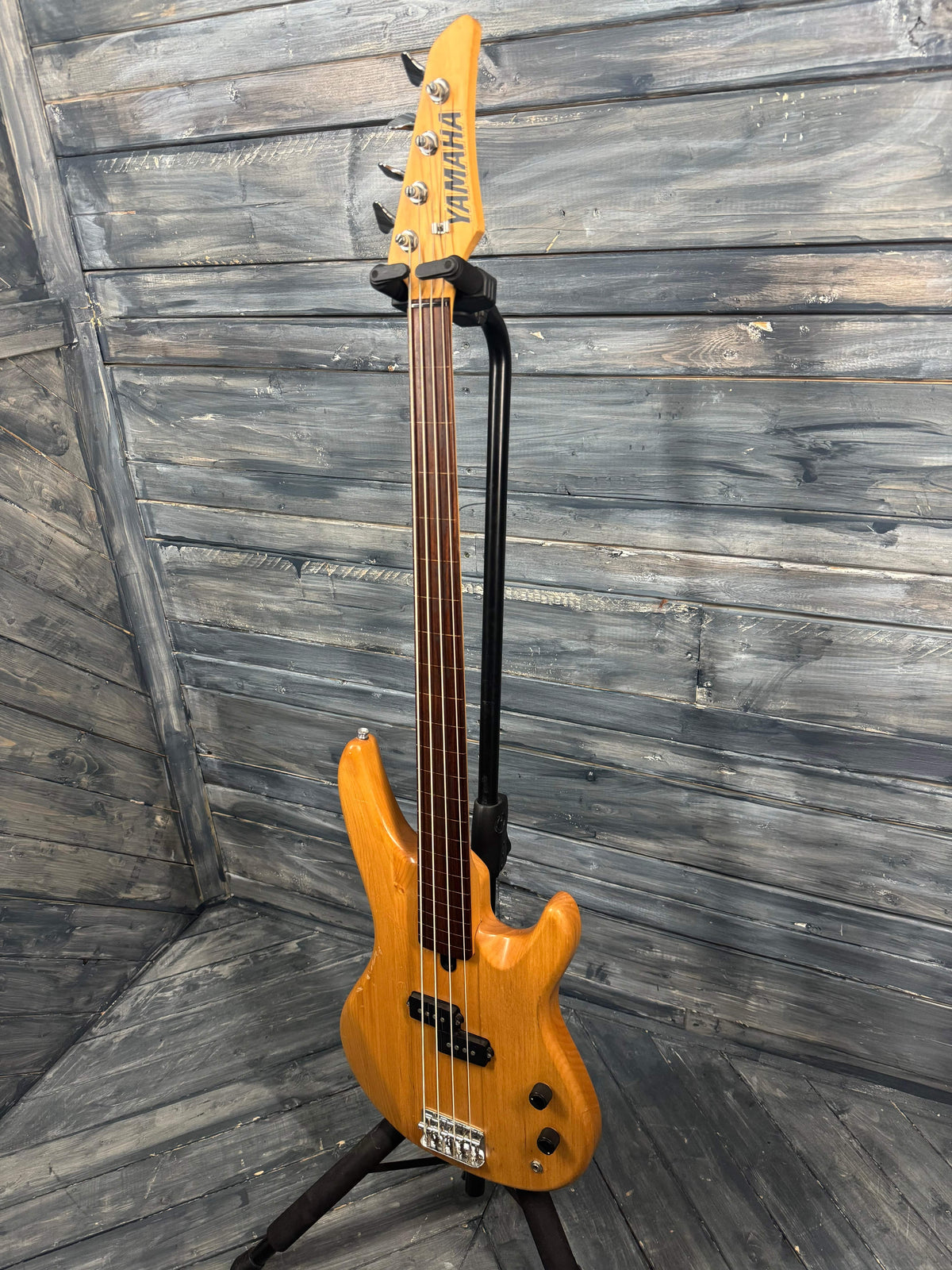 Yellow electric bass guitar leaning against a wooden wall.