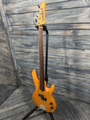 Yellow electric bass guitar leaning against a wooden wall.